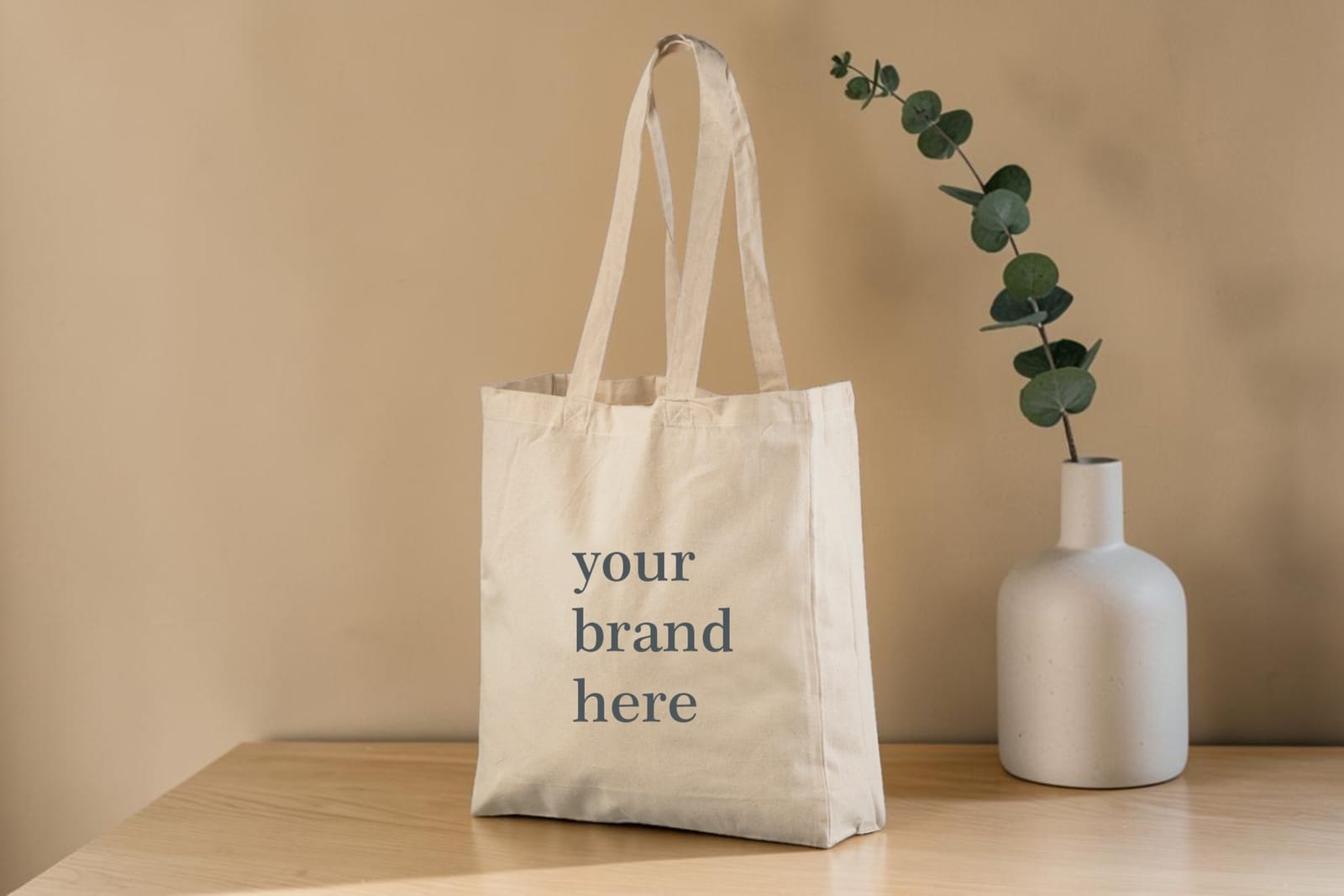 Bomullsnett med trykk – «your brand here» på et nett på trebord ved en hvit vase – natur.